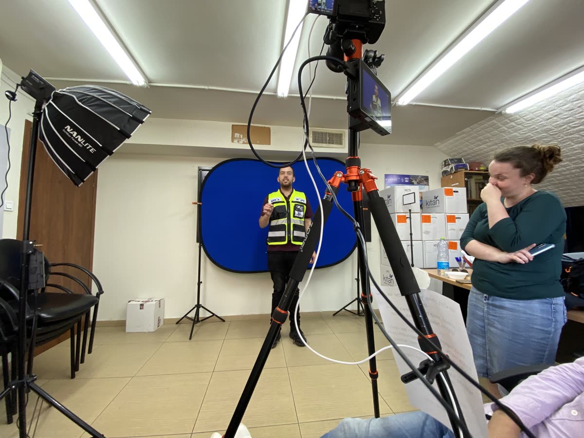 A Hatzalah volunteer in his green vest filmed against a blue backdrop