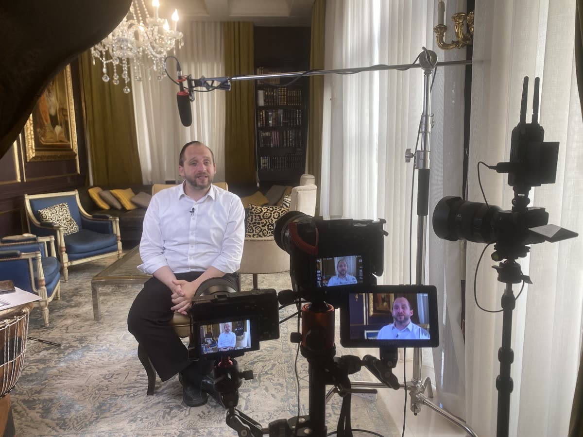 A man in a white shirt interviewed in a fancy living room, two monitors
