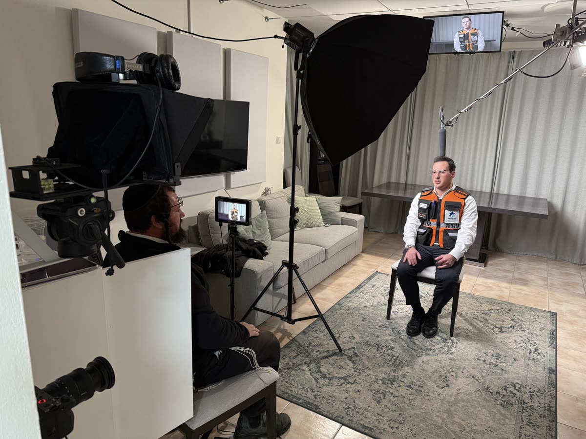 A United Hatzalah volunteer in his vest, interviewed under lights in a living room